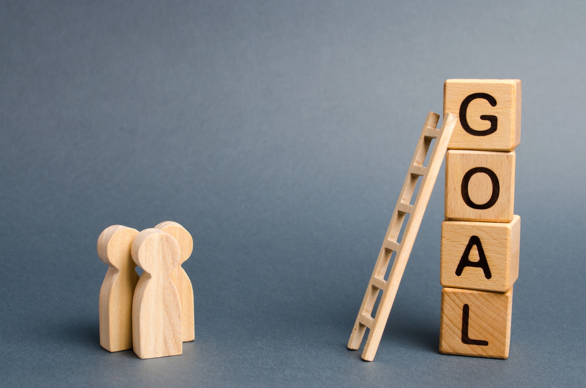 Three people are standing near the tower of cubes with the word goal